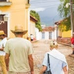 An older couple holding hands and walking down a cobblestone street in a vibrant Cuban town.