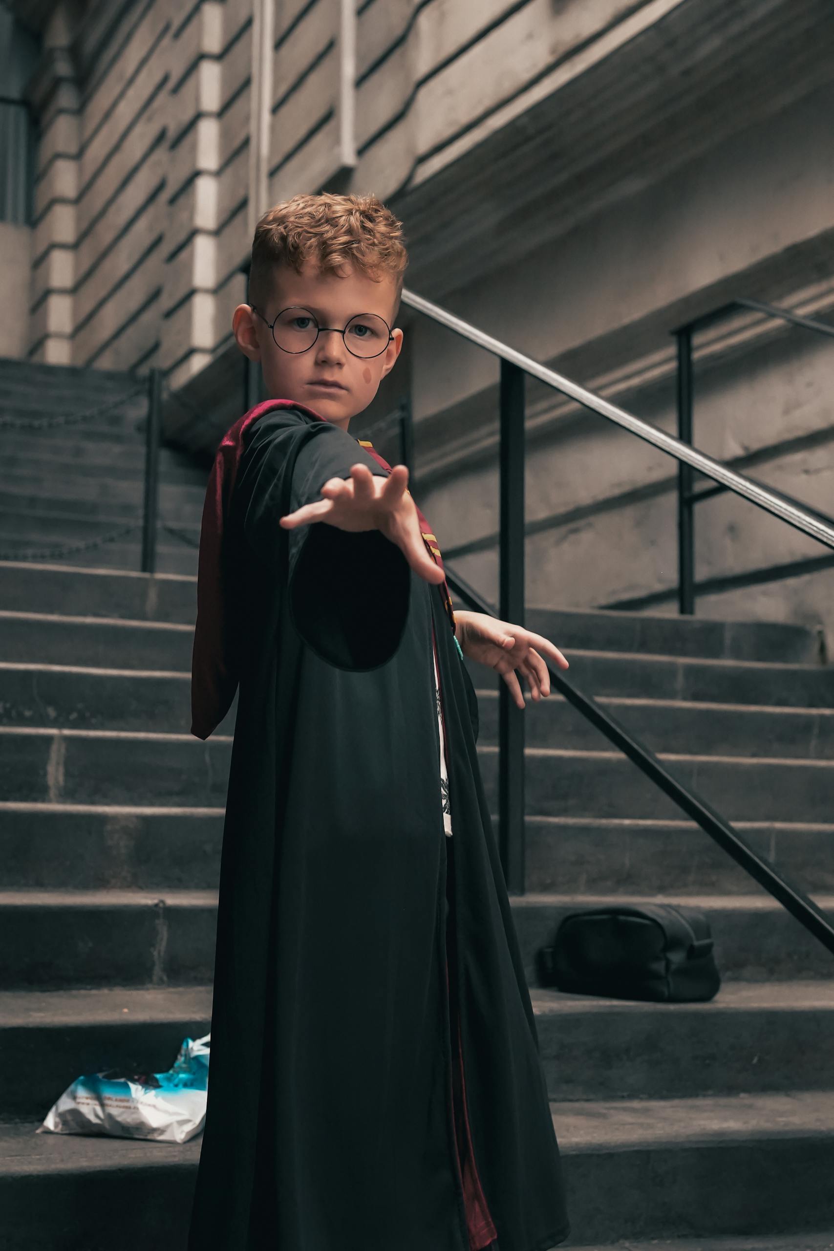 Child dressed as a wizard casting a spell on stone steps, resembling a scene from a fantasy film.
