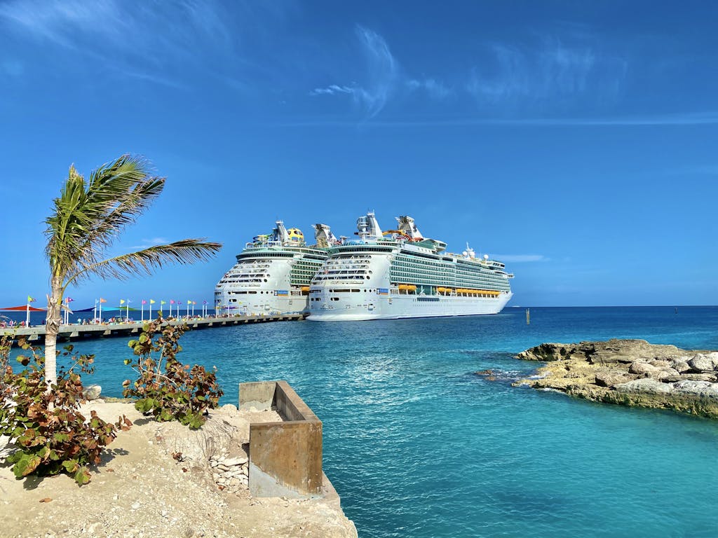 Similar big cruise ships sailing on rippled sea surrounded by small dry exotic islands and boardwalk under colorful blue sky in daylight in harbor